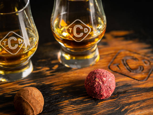 Close up of whisky & chocolate pairing, includes dram of whisky and round coated pink truffle chocolate